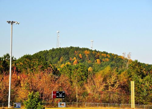 A hill covered in autumn foliage, with communication towers on top, surrounded by trees and a clear blue sky.