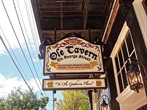 Sign for "Ole Tavern on George Street" featuring food, music, and games, with decorative elements and a blue sky backdrop.