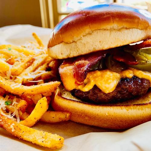 A juicy burger with bacon, cheese, and pickles, served with a side of crispy seasoned fries.