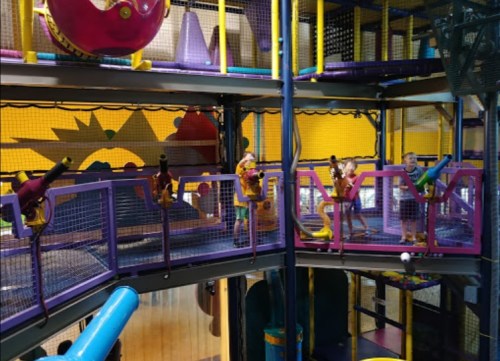 Children playing in a colorful indoor playground with climbing structures and interactive features.