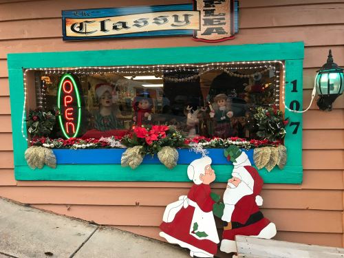 A festive storefront with a bright "Open" sign, holiday decorations, and cheerful Santa and Mrs. Claus cutouts.