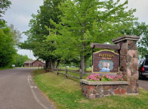 Sign for Pattison State Park at the entrance, surrounded by trees and a gravel road leading into the park.