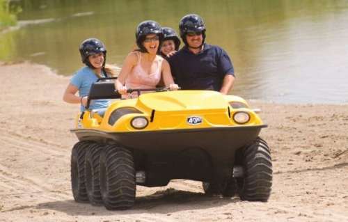 A group of four people joyfully riding an all-terrain vehicle on a sandy beach near a body of water.