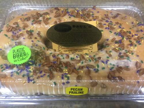 A king cake with icing, pecans, and colorful sprinkles, labeled "Paul's" and containing a plastic baby.