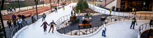 A bustling outdoor ice skating rink with people skating, sitting by a fire pit, and enjoying the winter atmosphere.