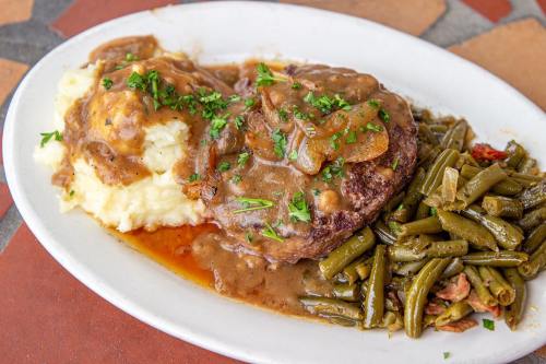 A plate of meatloaf topped with gravy, served with mashed potatoes and green beans, garnished with parsley.