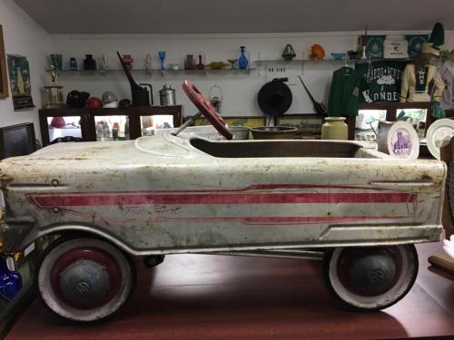 A vintage metal toy car with a red steering wheel, displayed on a wooden surface among various collectibles.