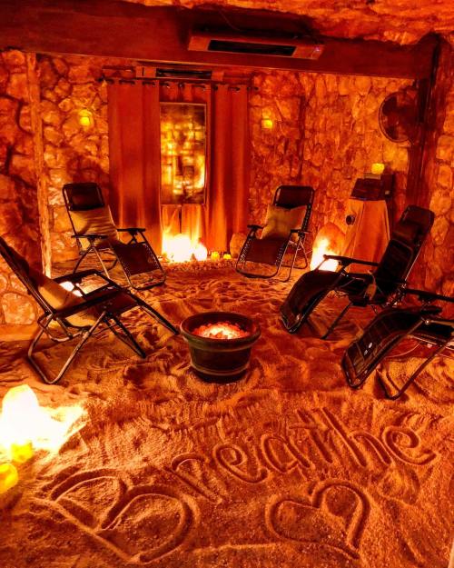 A cozy salt room with chairs, warm lighting, and "Breathe" written in the sand, creating a relaxing atmosphere.