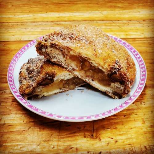 A plate with two pieces of sweet, cinnamon-sugar coated pastry filled with a gooey filling, resting on a wooden surface.
