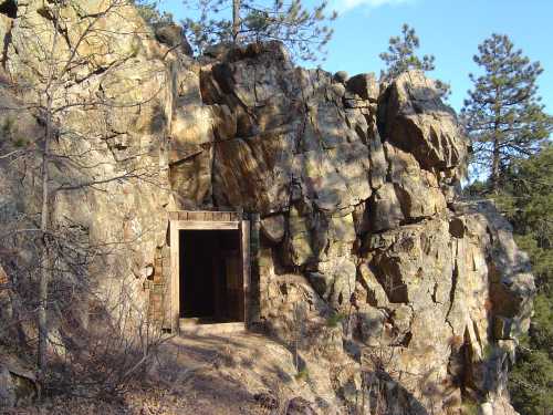 A rocky cliff with a wooden entrance to a cave or mine, surrounded by trees and blue sky.