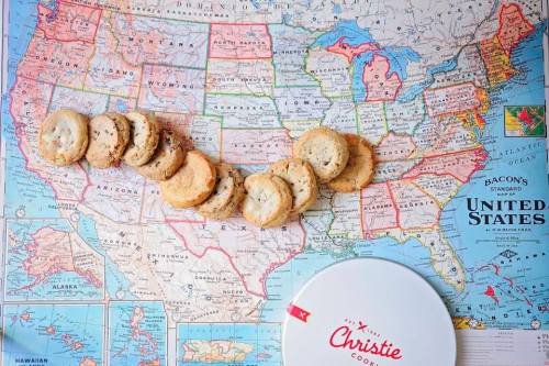 A map of the United States with a line of cookies placed across it, next to a round cookie tin.