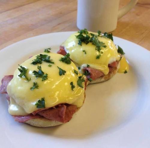 Two eggs Benedict on English muffins, topped with ham, hollandaise sauce, and fresh parsley, served on a white plate.
