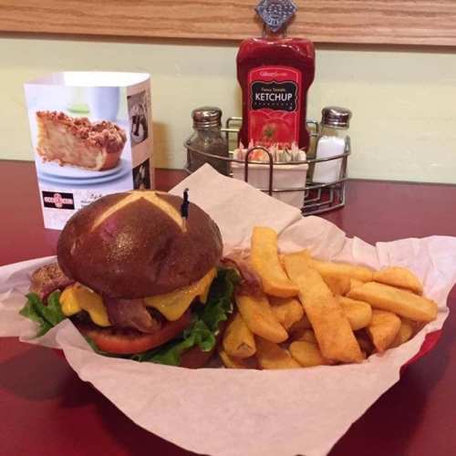 A pretzel bun burger with cheese, lettuce, and tomato, served with fries and ketchup on a red table.