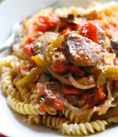 A plate of pasta topped with sausage, bell peppers, onions, and a rich tomato sauce.
