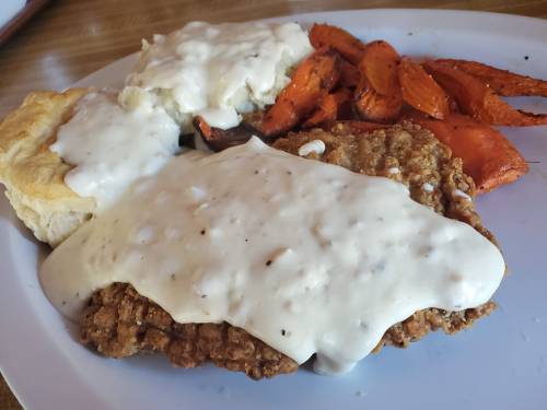 A plate featuring fried chicken smothered in white gravy, a biscuit, and roasted carrots.