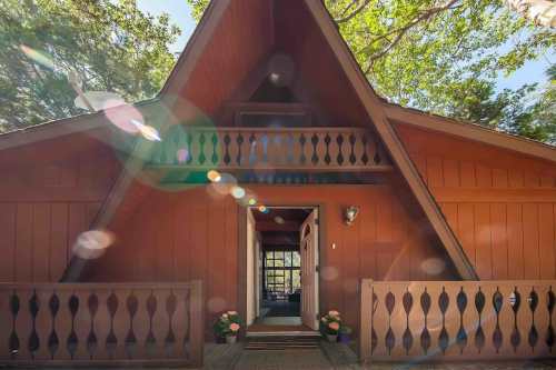 A charming A-frame cabin with a wooden exterior, surrounded by trees and sunlight, featuring a welcoming entrance.