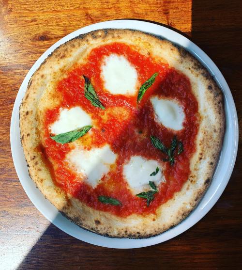 A round pizza with a golden crust, topped with tomato sauce, mozzarella, and fresh basil leaves.