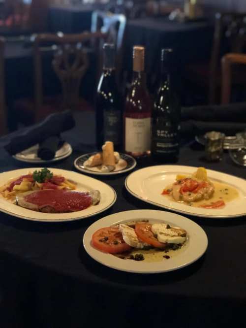 A table set with three gourmet dishes and bottles of wine, all elegantly arranged on a black tablecloth.
