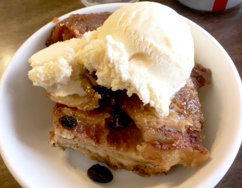 A bowl of warm bread pudding topped with a scoop of vanilla ice cream.