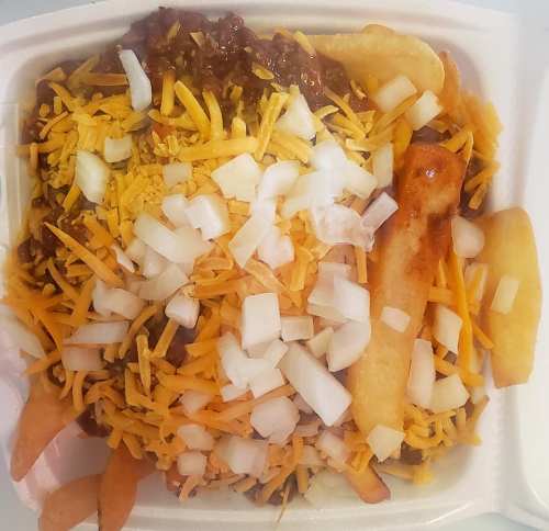 A container filled with fries topped with chili, shredded cheese, and diced onions.