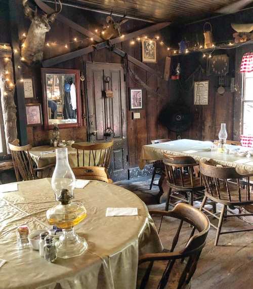 Cozy rustic dining room with wooden tables, chairs, and warm lighting, featuring vintage decor and a lantern centerpiece.