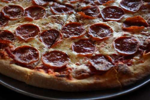A close-up of a pepperoni pizza with melted cheese and a golden crust on a dark plate.