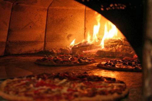 A wood-fired oven with pizzas baking inside, flames visible in the background.