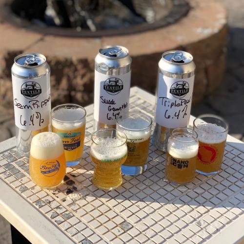 A table with three tall cans of beer and several small glasses of different beer types, labeled with their ABV percentages.