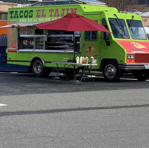 A vibrant green food truck named "Tacos El Tajin" with an umbrella and tables set up outside.