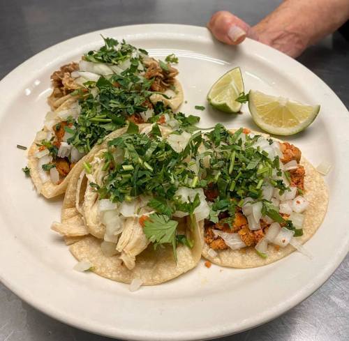 A plate of three tacos topped with onions, cilantro, and lime wedges, held by a hand.