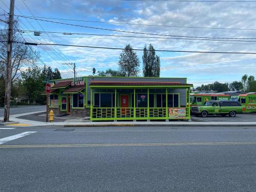 A colorful taco restaurant with green exterior and a red door, located on a street with parked food trucks nearby.