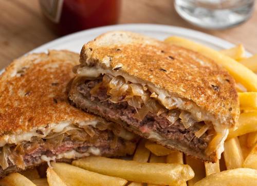 A close-up of a grilled sandwich filled with beef and onions, served with a side of golden French fries.