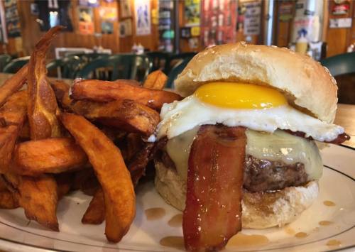 A juicy burger topped with a fried egg and bacon, served with a side of crispy sweet potato fries.