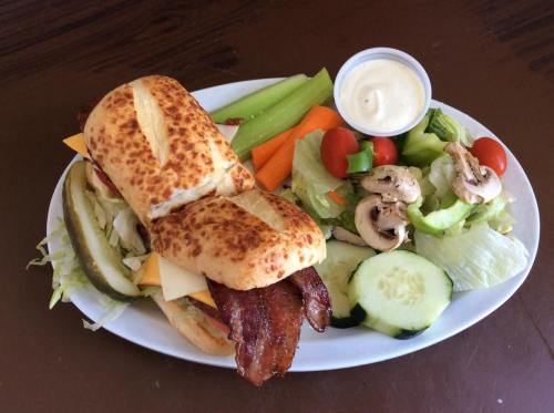 A sandwich with bacon and cheese, served with a side of salad, celery, carrots, and ranch dressing.