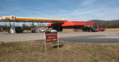 A gas station with a sign advertising chocolate rolls for sale, set against a rural landscape.