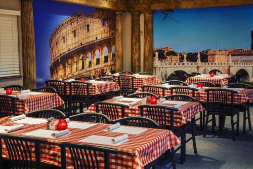 Cozy restaurant interior with checkered tablecloths, candlelit tables, and a mural of the Colosseum and bridge.