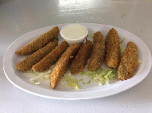 A plate of crispy fried pickles served with a small cup of dipping sauce on a bed of shredded lettuce.