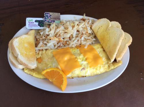 A plate with a cheese omelet, hash browns, toast, and an orange slice, accompanied by butter packets.