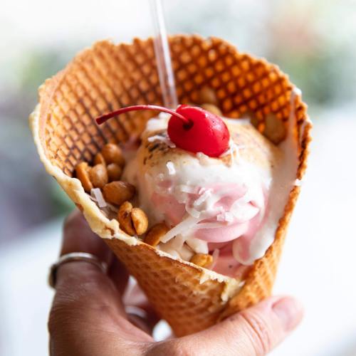 A hand holding a waffle cone filled with ice cream, topped with a cherry and nuts.
