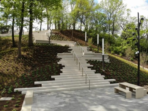 A landscaped area featuring white stairs leading up a hill, surrounded by trees and newly planted greenery.