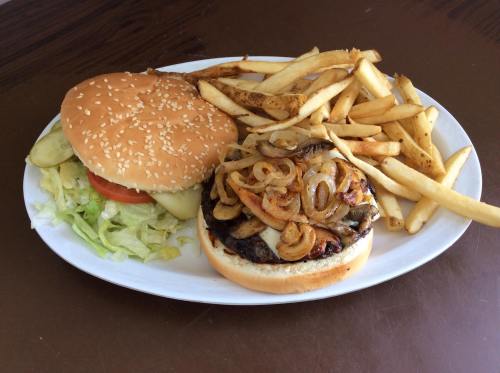 A plate with a sesame seed burger topped with grilled onions, lettuce, and tomato, served with a side of fries.