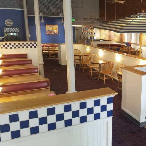 Interior of a restaurant featuring booths, wooden chairs, and blue and white checkered decor. Bright and spacious atmosphere.