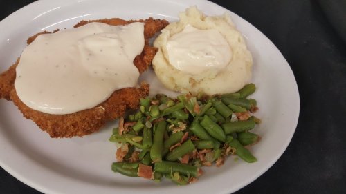 A plate featuring fried chicken with gravy, mashed potatoes, and green beans with bacon.