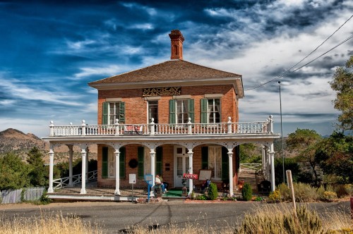 Historic Mackay Mansion with a porch, surrounded by mountains and a blue sky, featuring an "Open" sign.