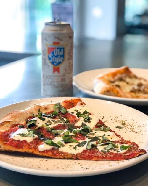 A slice of pizza topped with mozzarella and basil, next to a can of Old Style beer on a table.
