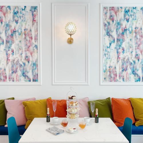 A cozy café setting with colorful cushions, a tiered dessert stand, and drinks on a marble table against vibrant wall art.