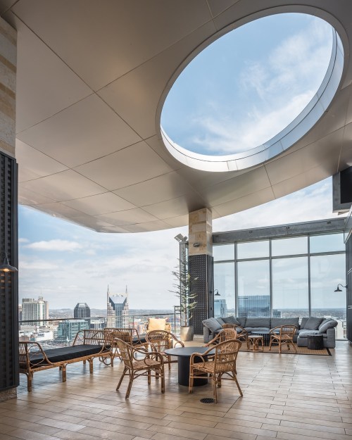A modern rooftop lounge with circular skylight, featuring stylish seating and a panoramic city view.