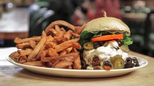 A delicious burger topped with lettuce, olives, and peppers, served with a side of crispy fries on a plate.