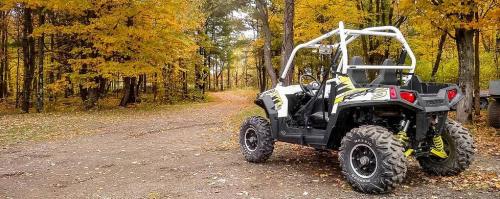A side-by-side ATV parked on a dirt path surrounded by autumn trees with vibrant yellow leaves.