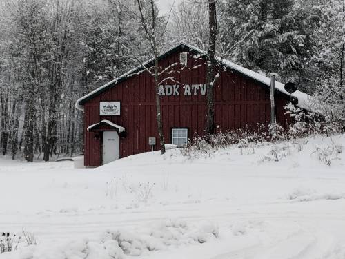 A red barn-like building labeled "ADK ATV" surrounded by snow-covered trees and ground.